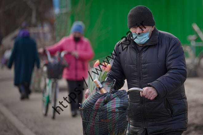 مردی کیسه‌ها و دسته‌ای گل لاله را با دوچرخه در استانیتسیا لوهانسکا، تنها گذرگاهی که روزانه باز است، در منطقه لوهانسک، شرق اوکراین، در فوریه حمل می‌کند.  22، 2022.
